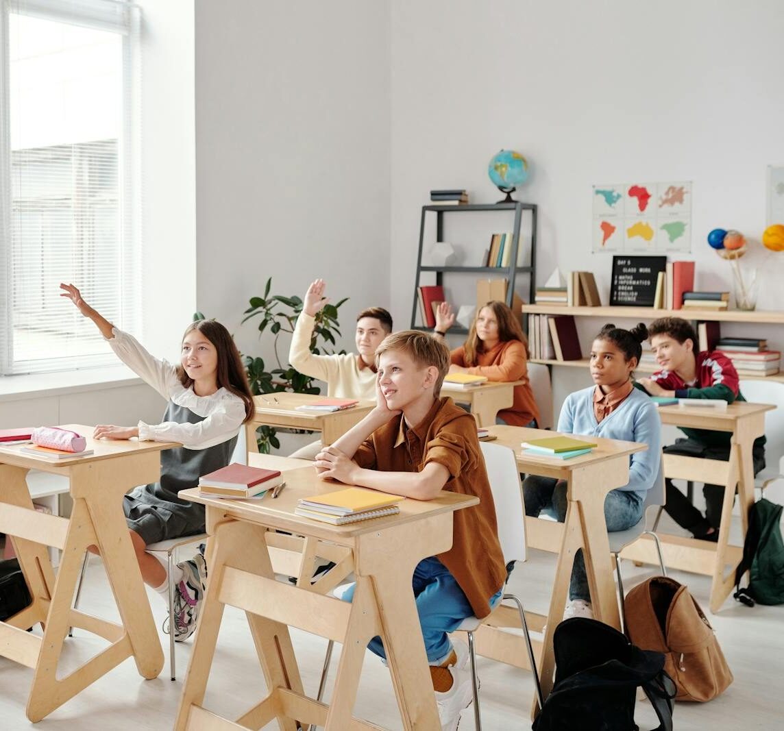 Students engage eagerly in a classroom, raising hands and participating in a lesson with their teacher.