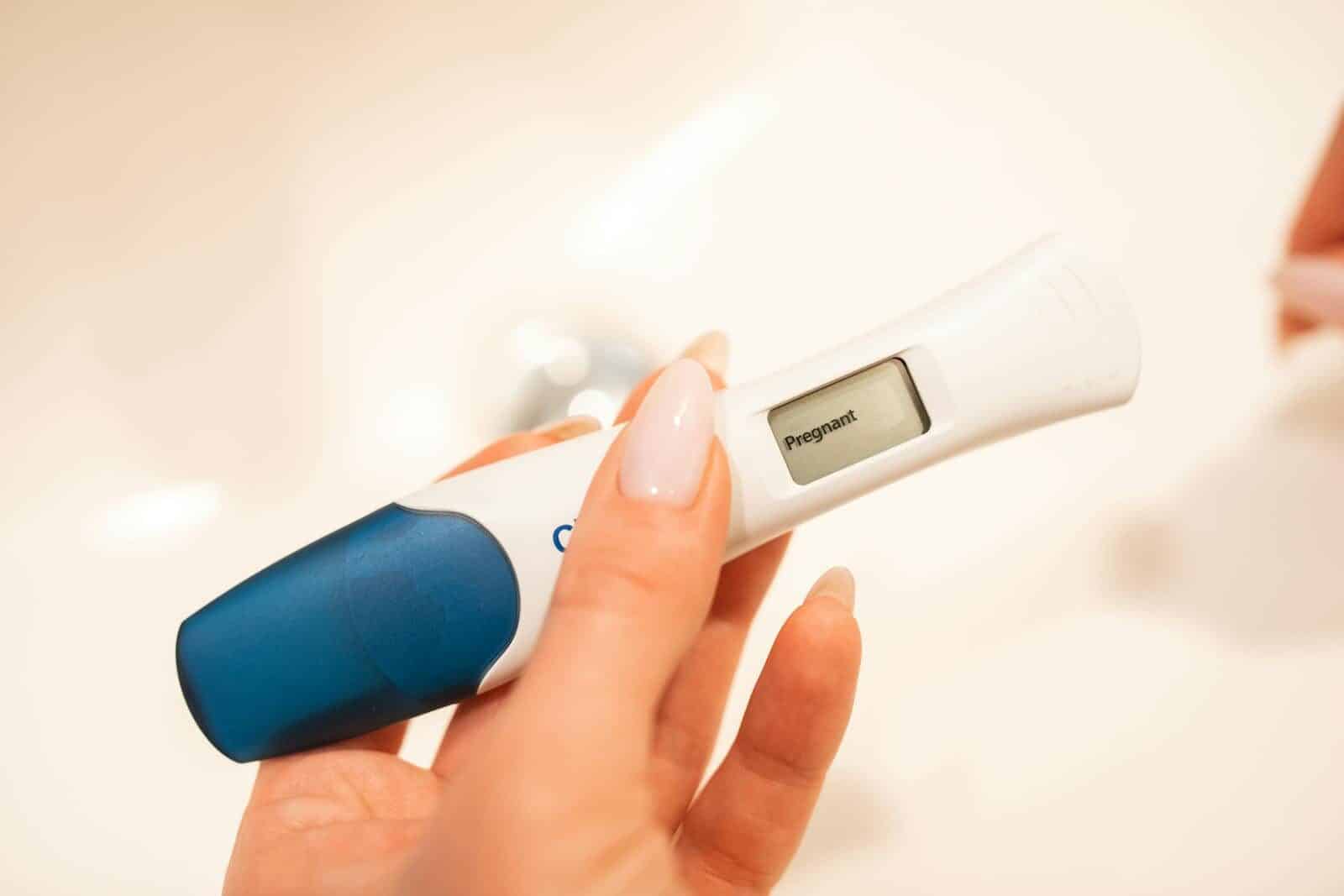 Close-up view of a positive digital pregnancy test held by a woman with manicured nails.
